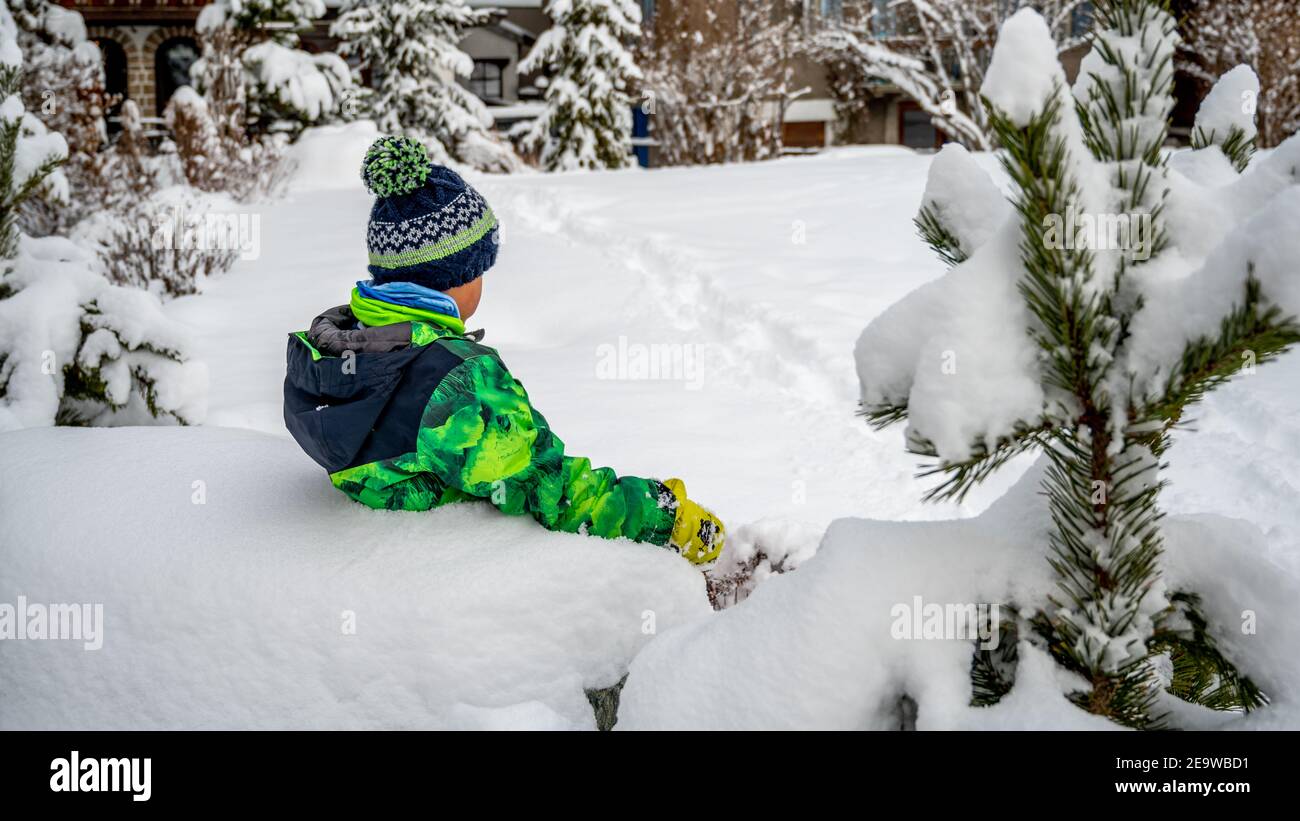 Bambino che gioca nella neve. Un ragazzo asiatico in abbigliamento da sci seduto in inverno. Felice infanzia e divertente. Zermatt, Svizzera. Foto Stock