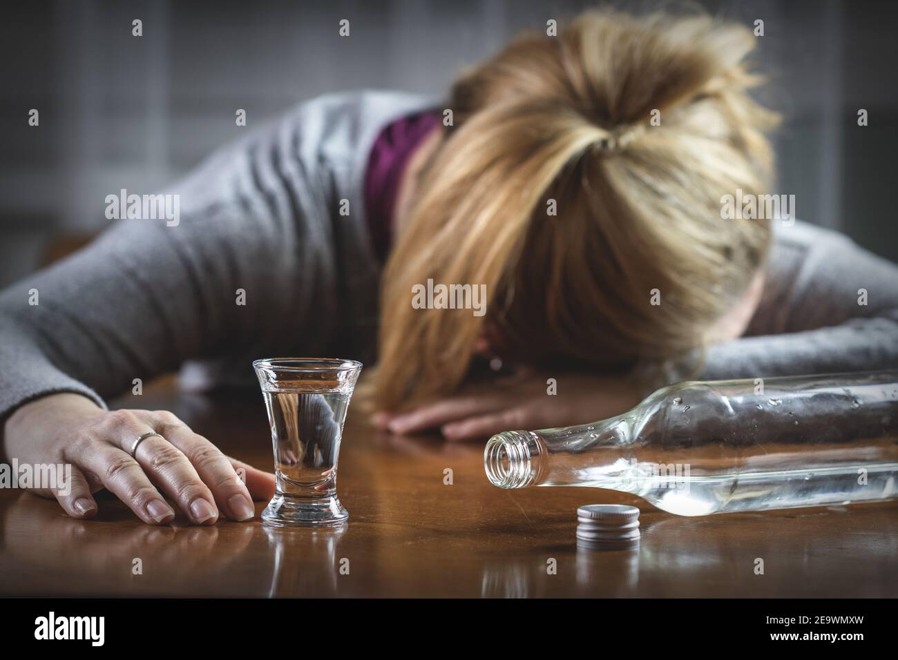 Donna ubriaca che dorme sul tavolo dopo aver bevuto la vodka. Concetto di abuso di alcool. Liquore duro in vetro e bottiglia Foto Stock