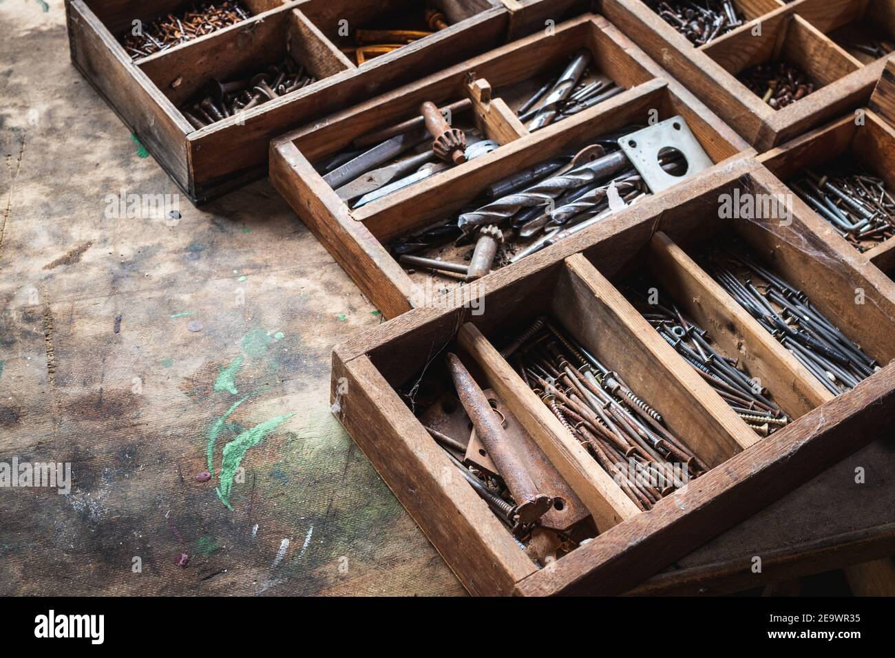 Cassetta attrezzi con chiodo, bullone, viti e punta da trapano su tavola in legno. Attrezzature industriali arrugginite in officina di carpenteria Foto Stock