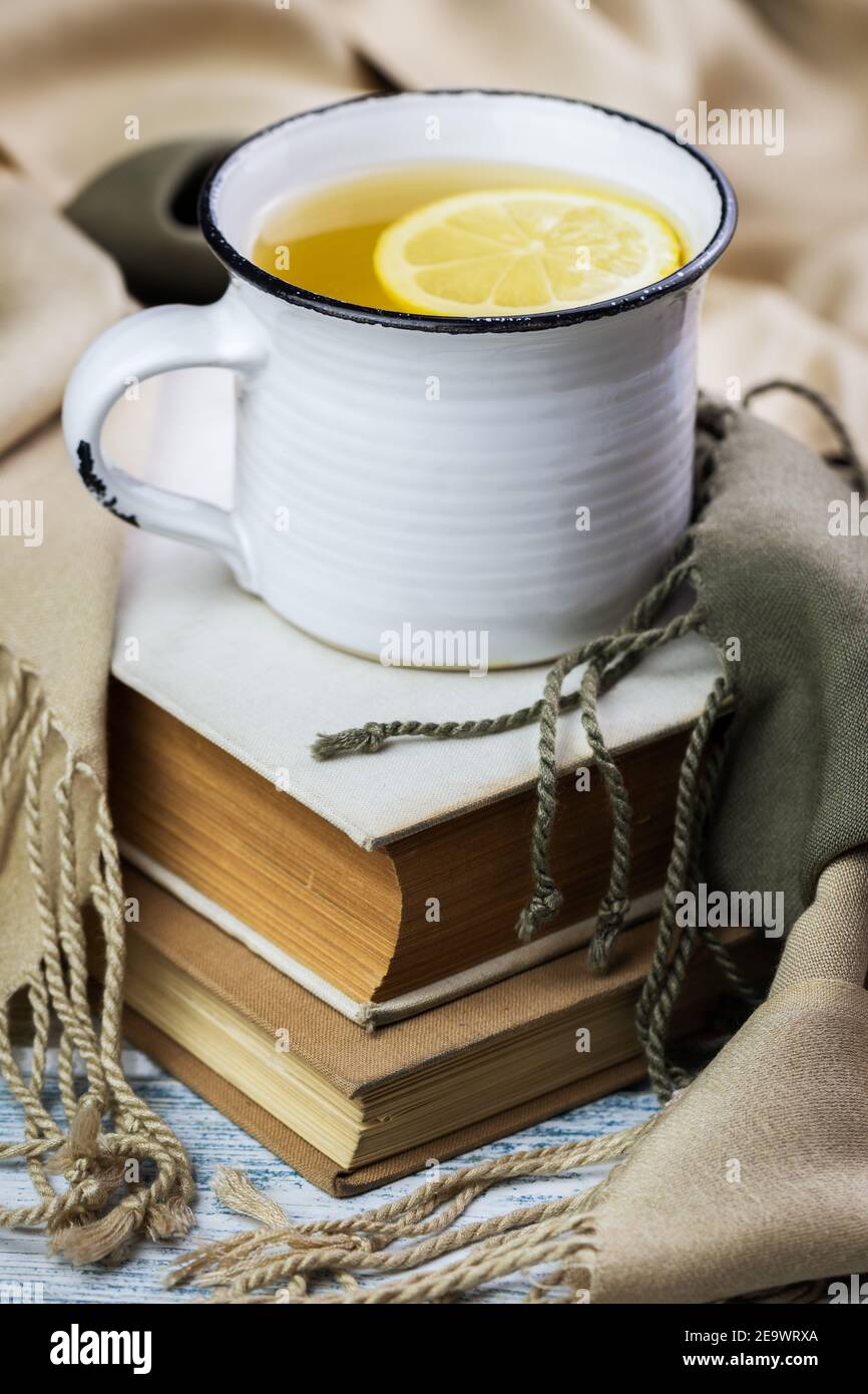 Bevanda calda del tè in tazza su libri che coprono da sciarpa. Ancora vita di teacup su vecchio libro. Rinfresco durante la lettura Foto Stock