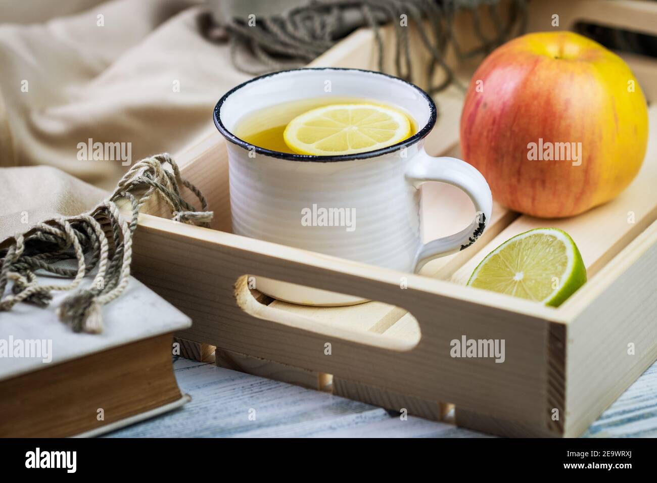Tè caldo sul vassoio con mela e limone. Colazione o rinfresco sano. Ancora vita con libro e sciarpa sul tavolo Foto Stock