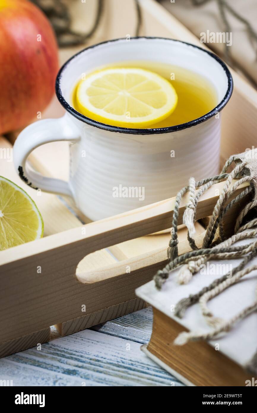 Tè caldo sul vassoio con mela e limone. Colazione o rinfresco sano. Ancora vita con libro e sciarpa sul tavolo Foto Stock
