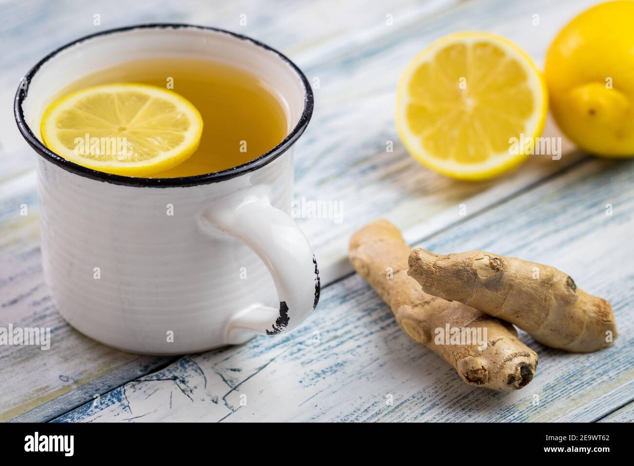 Tè allo zenzero con fetta di limone in tazza bianca. Concetto di stile di vita sano. Bevanda calda in teacup e radice di zenzero su tavolo di legno Foto Stock