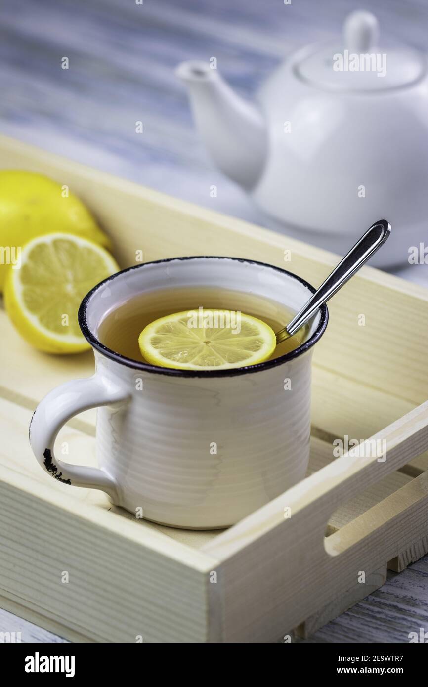 Bevanda a base di tè con fetta di limone in tazza bianca e teiera. Bevanda calda sul vassoio da portata su un tavolo di legno bianco. Rinfresco alla prima colazione del mattino Foto Stock