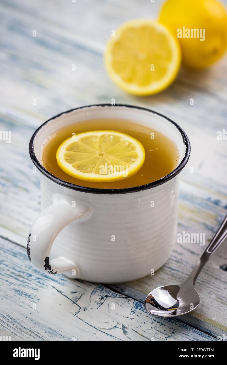 Tè con fetta di limone in teacup bianco. Tazza e cucchiaio su tavolo di legno. Bevande calde rinfrescanti Foto Stock