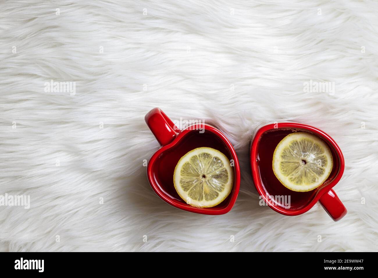 Due tazze da tè a forma di cuore rosso con fetta di limone su fondo di pelliccia. Casa dolce casa. Bevanda calda al giorno delle valentine Foto Stock