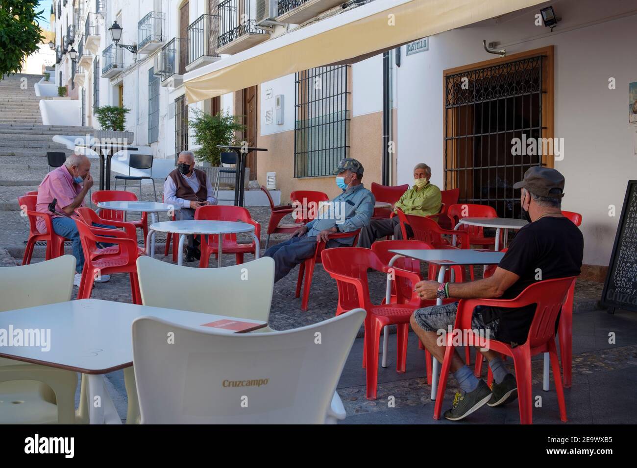 Anziani maschi residenti in maschera, seduti fuori dal bar del villaggio chiuso durante la pandemia di Covid nell'estate 2020. Carcabuey, Andalusia, Spagna Foto Stock