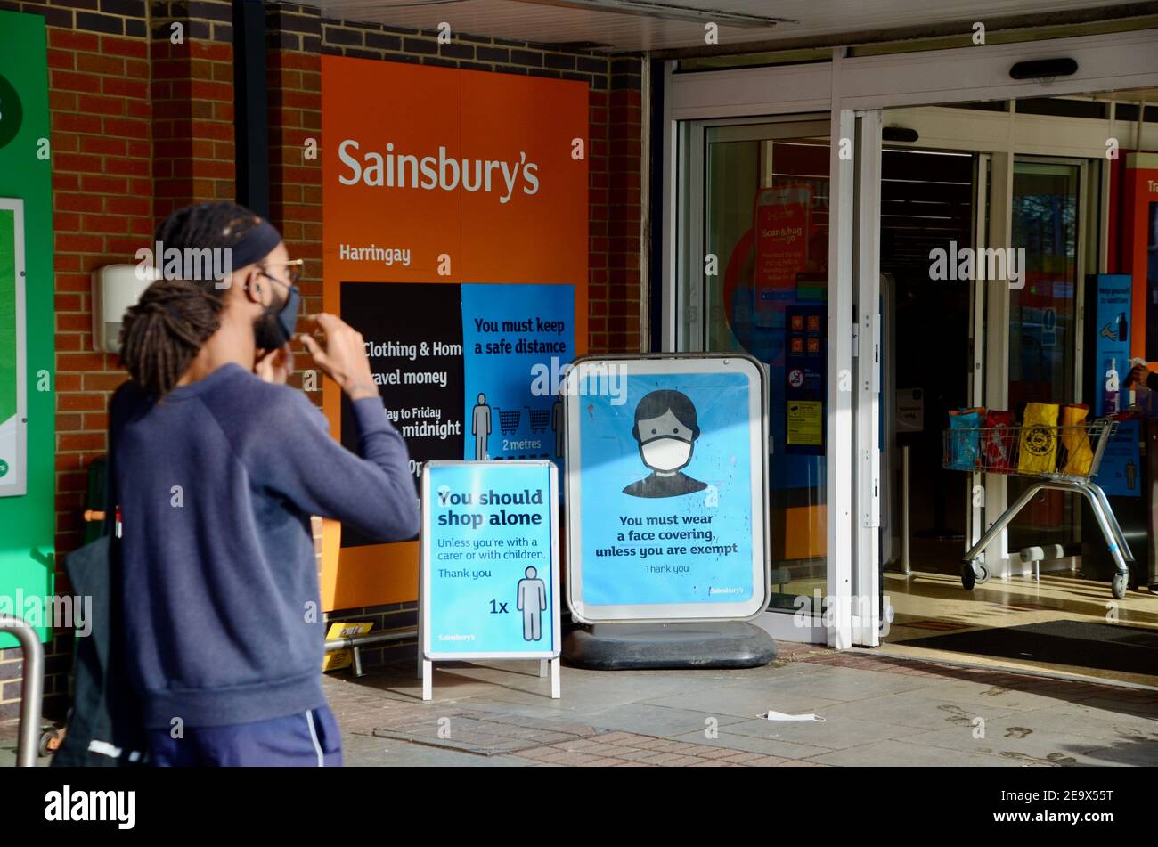 Uomo che mette sulla maschera fuori Sainsbury's haringey london con maschera cartelli e acquirenti Foto Stock