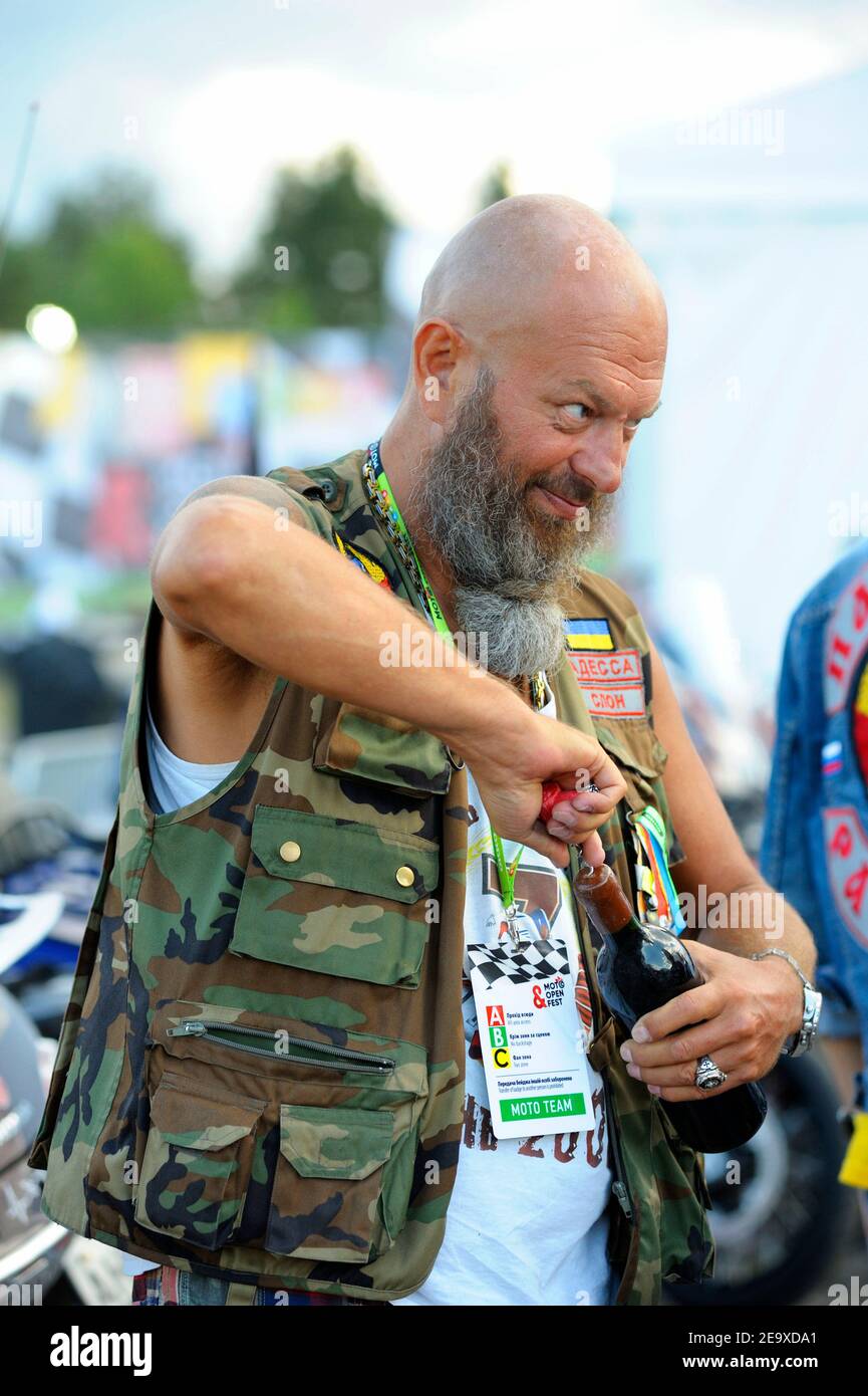 Bearded uomo biker aprire una bottiglia di vino che celebra l'inizio di motociclisti rally Foto Stock