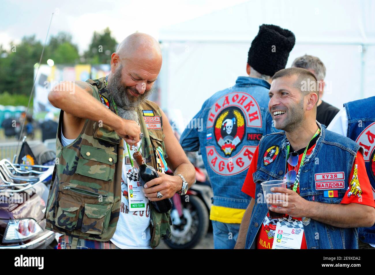 Bearded uomo biker aprire una bottiglia di vino che celebra l'inizio di motociclisti rally Foto Stock
