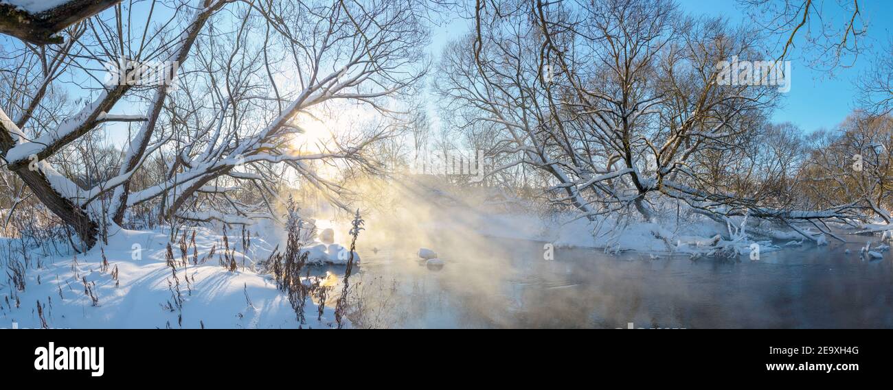 Paesaggio panoramico invernale gelido con fiume forestale durante la soleggiata mattina di gennaio. Foto Stock