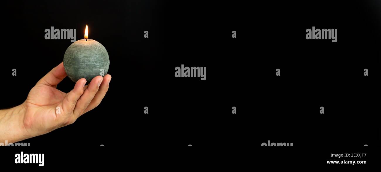 Uomo che tiene la candela rotonda che brucia su sfondo scuro, banner con spazio di copia Foto Stock