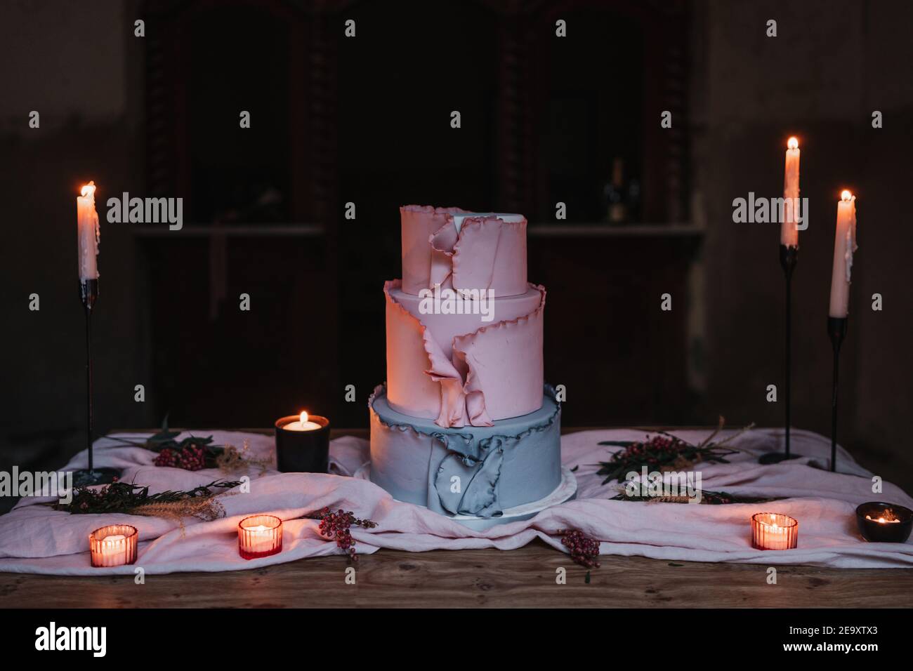 Deliziosa torta a più livelli servita su un tavolo di legno e circondata da candele bruciate in camera buia Foto Stock