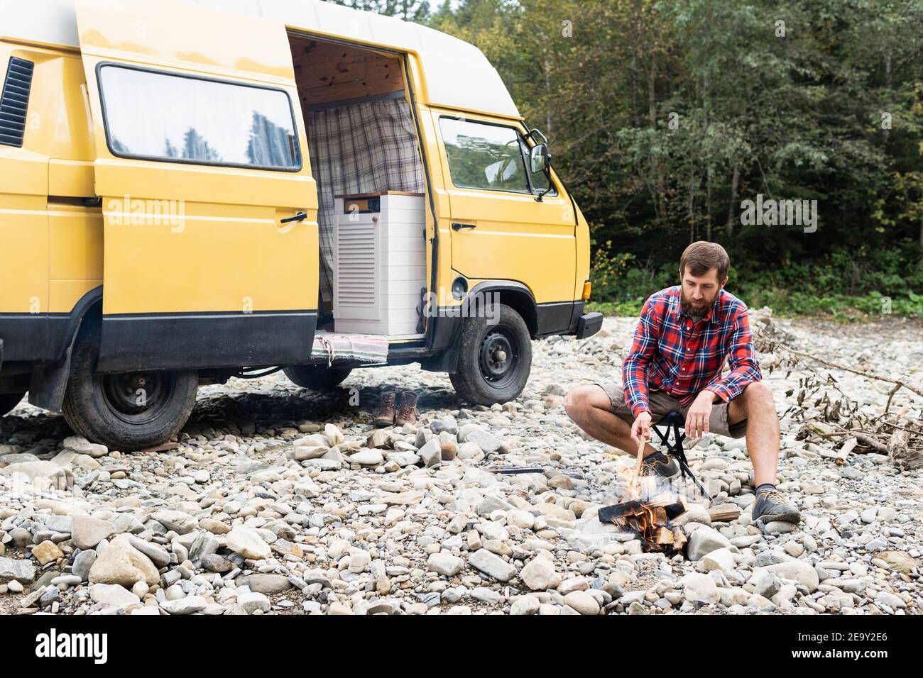 Giovane uomo che viaggia in un camper giallo attraverso la campagna. Campeggio off-grid auto-costruito in campeggio nella natura selvaggia. Foto Stock