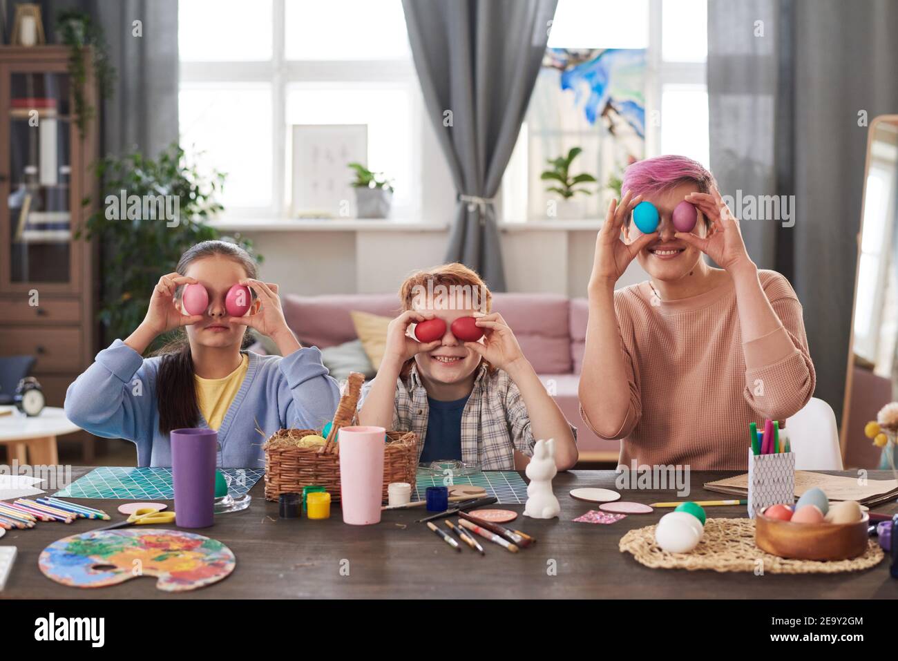 Ritratto di famiglia di tre seduti al tavolo e. tenendo le uova colorate davanti ai loro volti Foto Stock