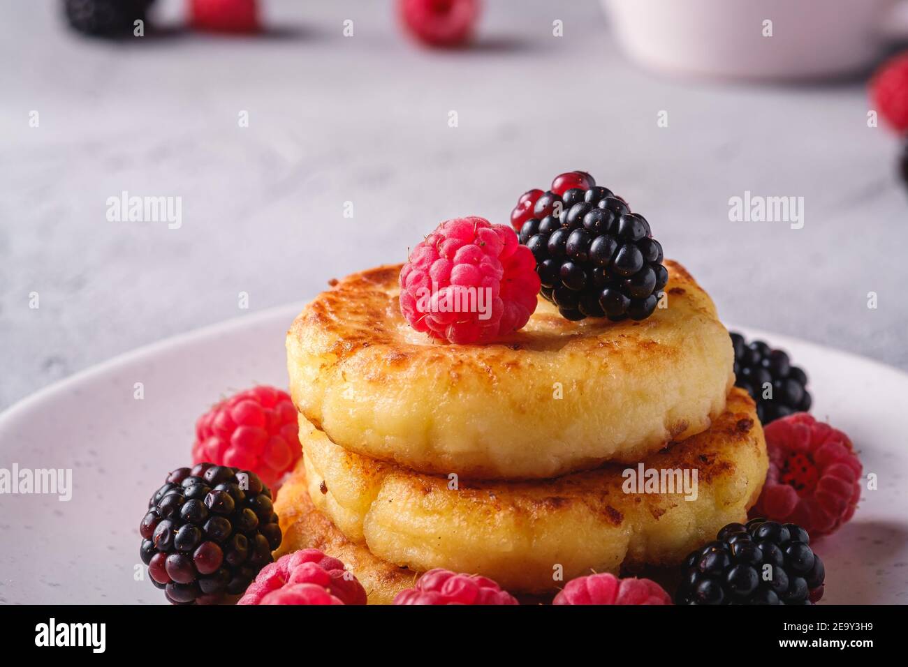 Frittelle al formaggio di cottage, frittelle di cagliata dessert con lampone e frutti di mora in piastra su fondo di pietra in cemento, macro angolo vista Foto Stock