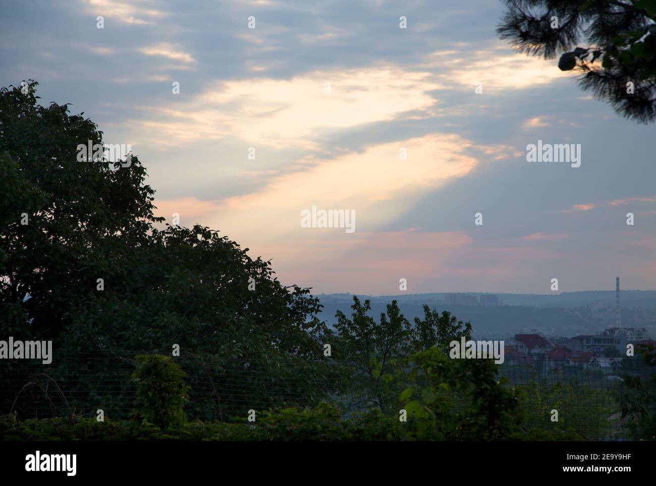 I raggi del sole strisciano attraverso il cielo blu da dietro le nuvole retroilluminate. La vista a Chisinau da una collina. Foto Stock