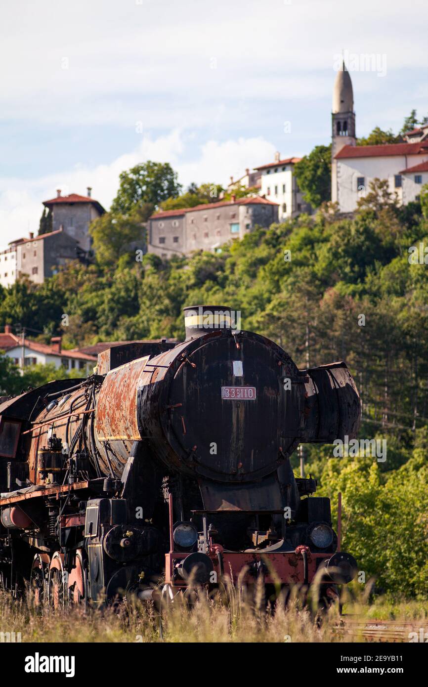Una vecchia locomotiva nera a vapore accanto al vecchio villaggio di Štanjel nel Carso sullo sfondo. Foto Stock