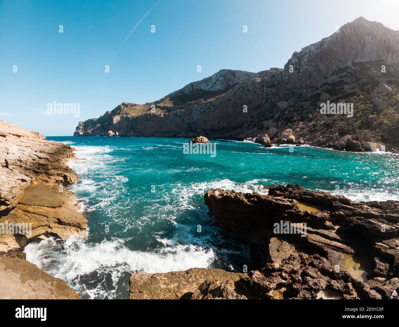 Onde che si infrangono sulla costa rocciosa delle montagne di Maiorca sullo sfondo, giornata di sole, nelle isole Baleari, Spagna Foto Stock