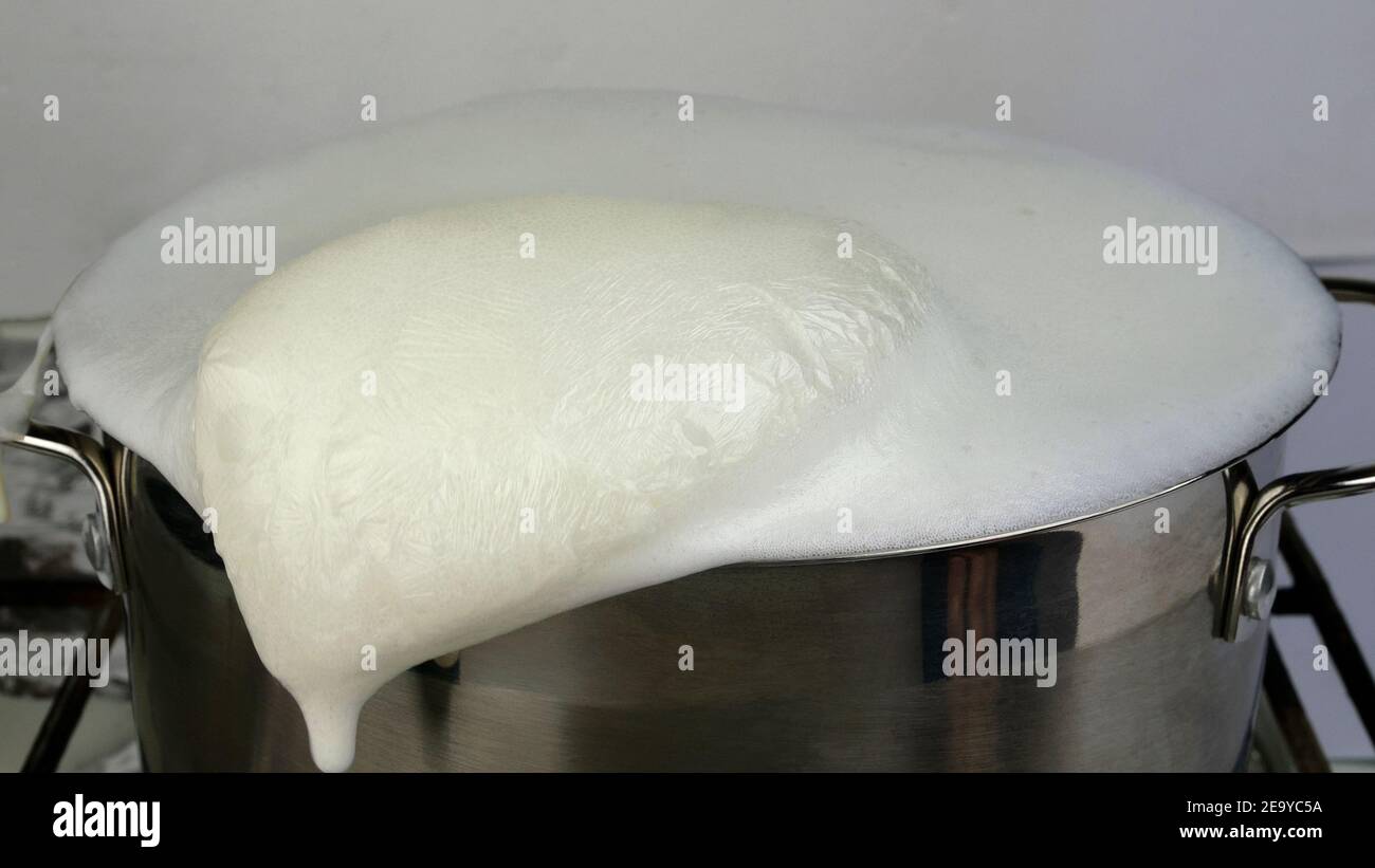Latte di mucche bollito e traboccante. Il latte bollente fuoriesce dalla pentola. Latte dimenticato sulla stufa. Messa a fuoco selettiva. Foto Stock