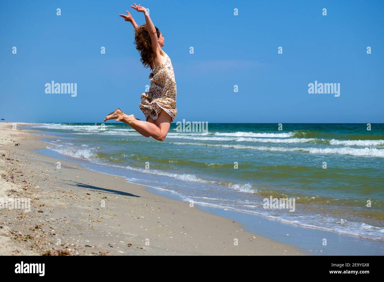 Ragazza giovane in un abito floreale si è congelata in un salto sullo sfondo del mare e del cielo blu Foto Stock