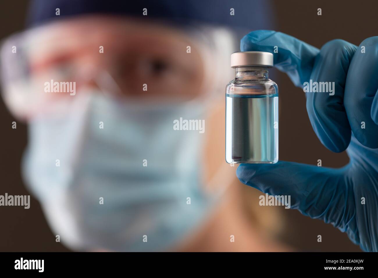 Femmina di lavoro medico che tiene il flaconcino del vaccino che indossa la maschera protettiva del viso e gli occhiali di protezione. Foto Stock