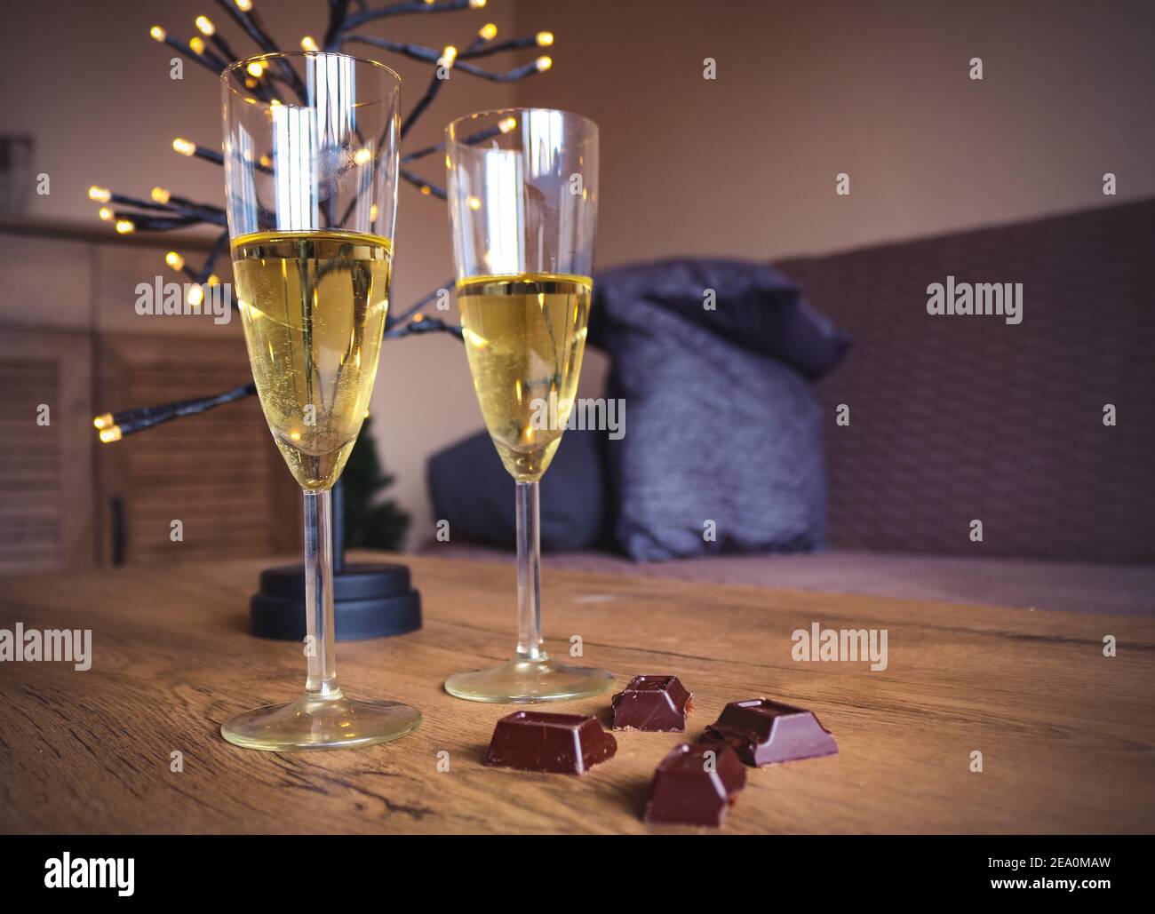 Due bicchieri di vino bianco, cioccolato e luci per una festa a casa Foto Stock