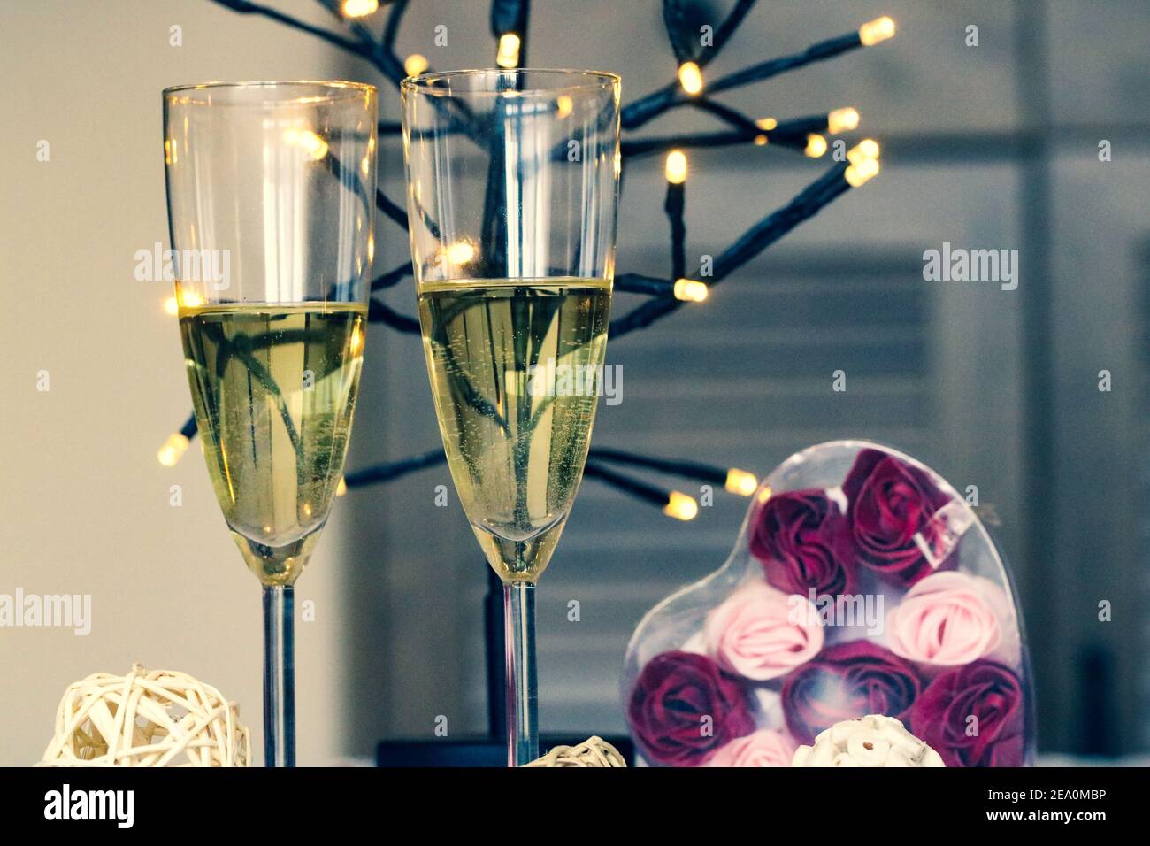 Due bicchieri di vino bianco, luci e regalo a forma di cuore per una celebrazione a casa Foto Stock