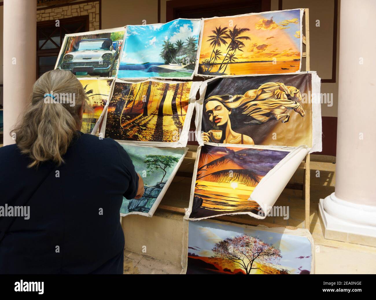 Cayo Santa Maria, Cuba, Febbraio 2016 - Vista posteriore di donna guardando con interesse a dipinti locali esposti per la vendita al di fuori di un negozio d'arte Foto Stock