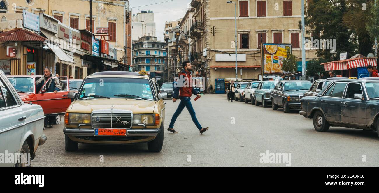 Un vecchio taxi Mercedes parcheggiato in strada, mentre un giovane attraversa la strada nella città di Tripoli, Libano Foto Stock