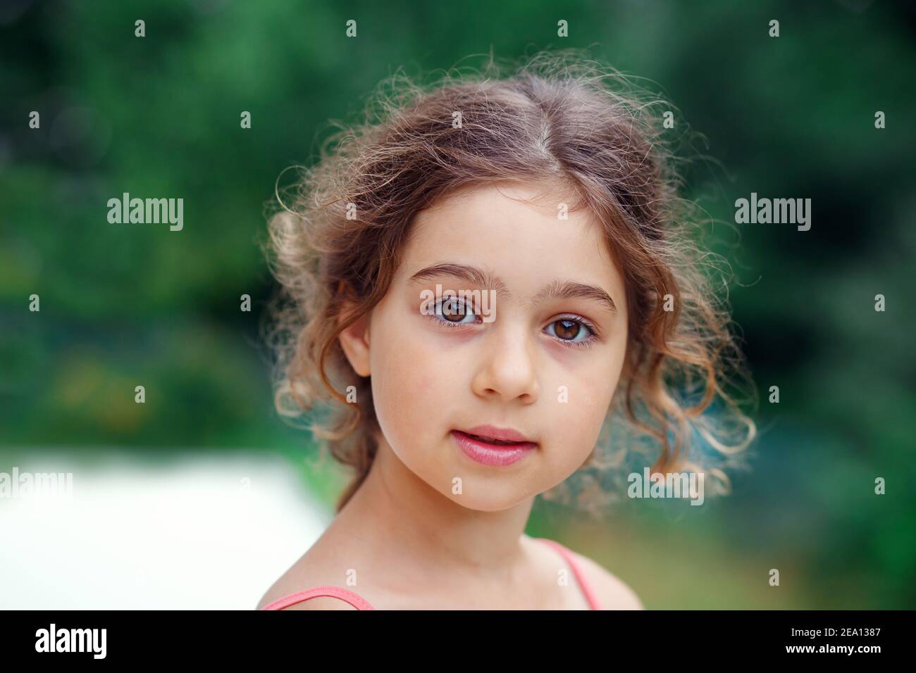 Ritratto di sorridente bella bambina al verde del parco estivo. Felice capretto che guarda la macchina fotografica Foto Stock