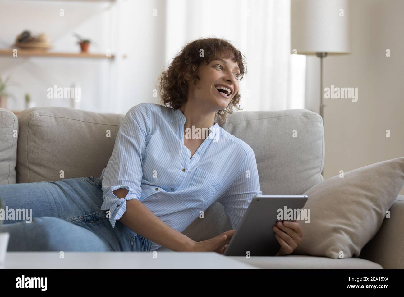 Donna felice riposa sul divano che naviga tablet Foto Stock
