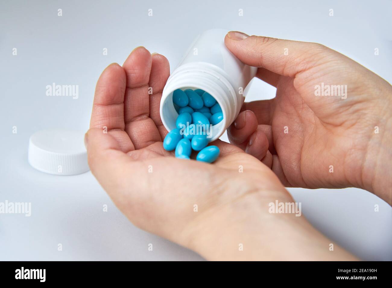 Una donna versa le pillole blu da un vaso di plastica nel palmo su uno sfondo bianco. Foto Stock