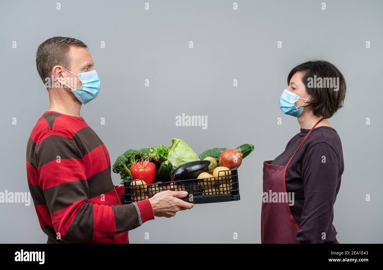 L'uomo che ottiene consegnato un cestino di prodotti da una donna. Entrambi indossano maschere. Consegna durante la pandemia di Covid. Foto Stock