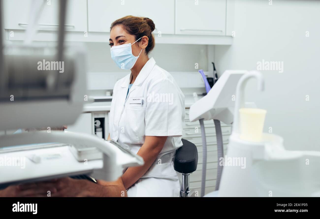 Donna medico indossando maschera viso seduta in clinica e paziente di esame. Dentista femminile seduto su una sedia e che controlla un paziente. Foto Stock