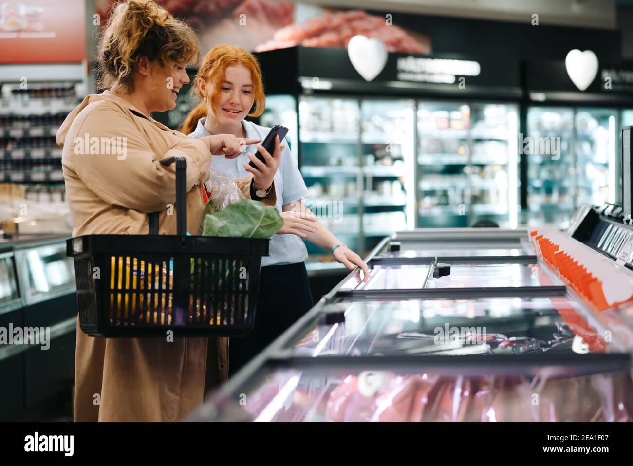 Cliente femminile che mostra l'elenco degli alimentari sul suo telefono ad un assistente del negozio. Shopper che prende aiuto da una lavoratrice femminile nel supermercato. Foto Stock