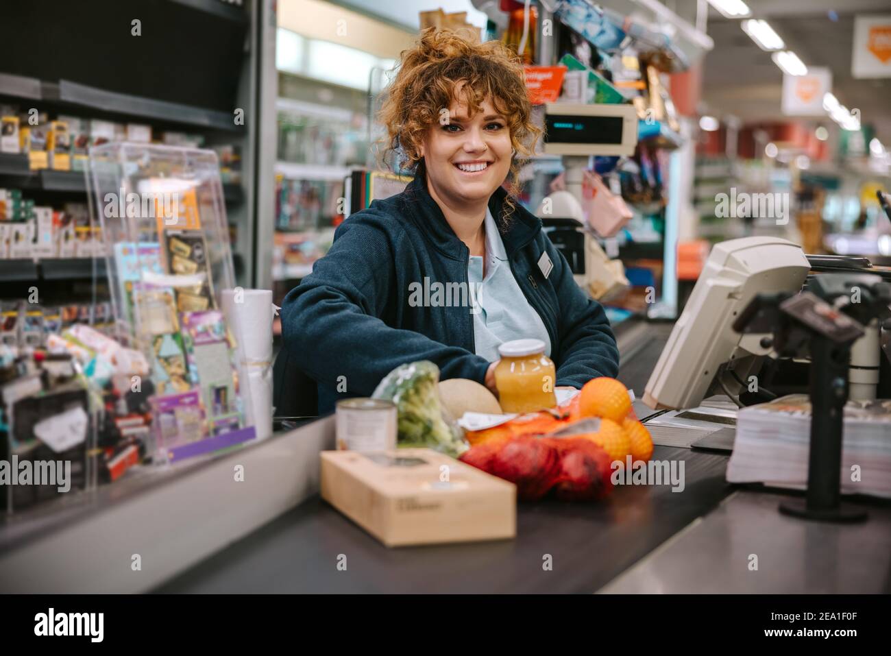 Ritratto di una donna seduta dietro il banco cassa sorridente alla fotocamera. Cassa supermercato al check-out. Foto Stock