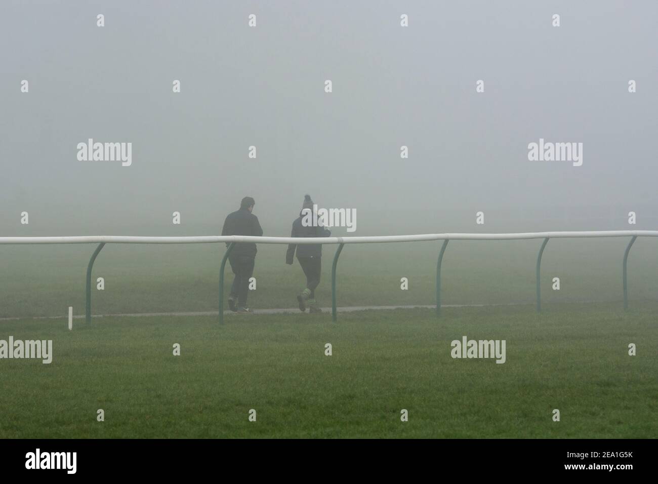 Persone che camminano nella nebbia invernale durante il blocco pandemico Covid-19, Warwick Racecourse, Warwickshire, Regno Unito. Febbraio 2021. Foto Stock