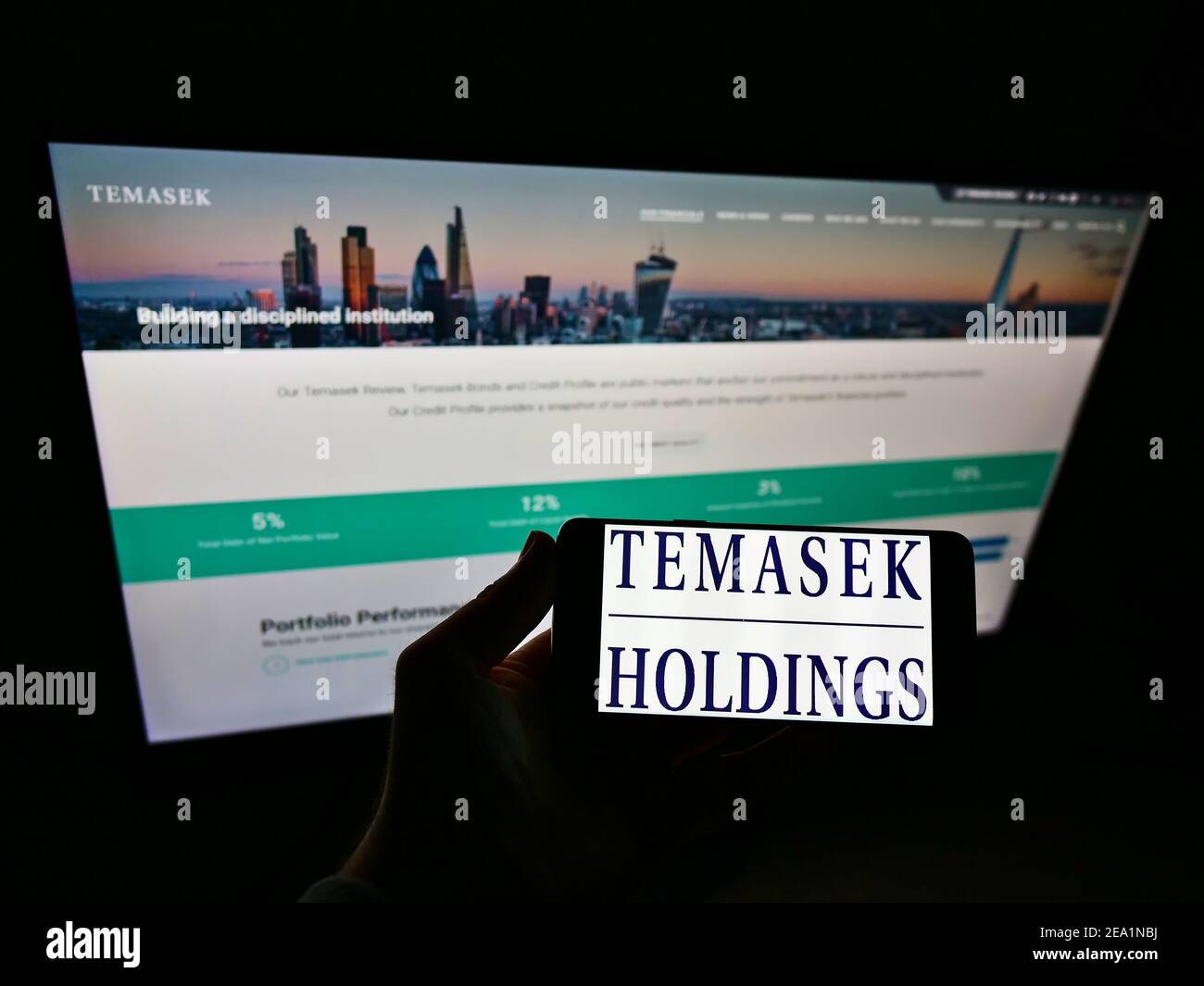 Persona che detiene il cellulare con il logo commerciale della società di investimenti singaporiani Temasek Holdings sullo schermo di fronte al sito web. Mettere a fuoco il display del telefono. Foto Stock