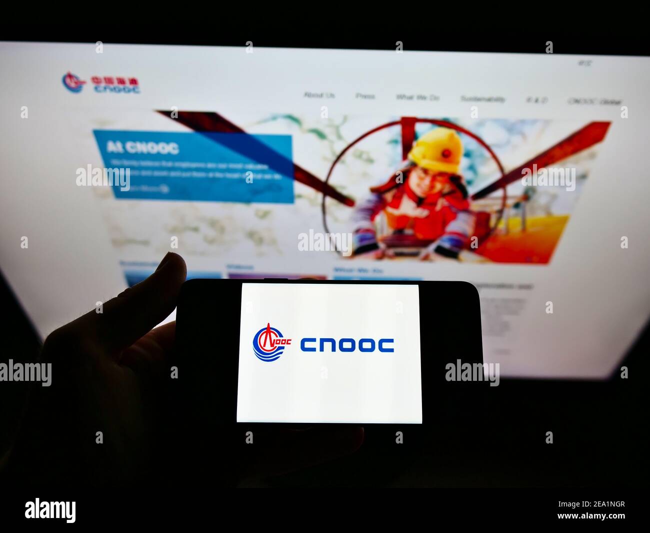 Persona in possesso di smartphone con logo della China National Offshore Oil Corporation (CNOOC) sullo schermo davanti al sito Web. Mettere a fuoco il display del telefono. Foto Stock