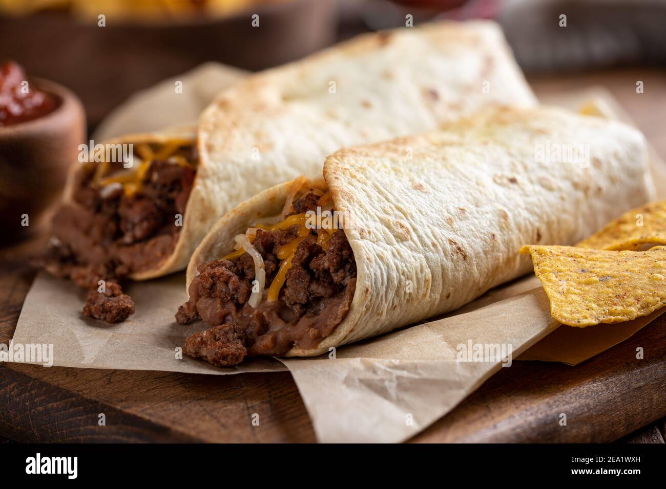 Burritos con manzo macinato, fagioli fritti e formaggio su un tagliere di legno Foto Stock