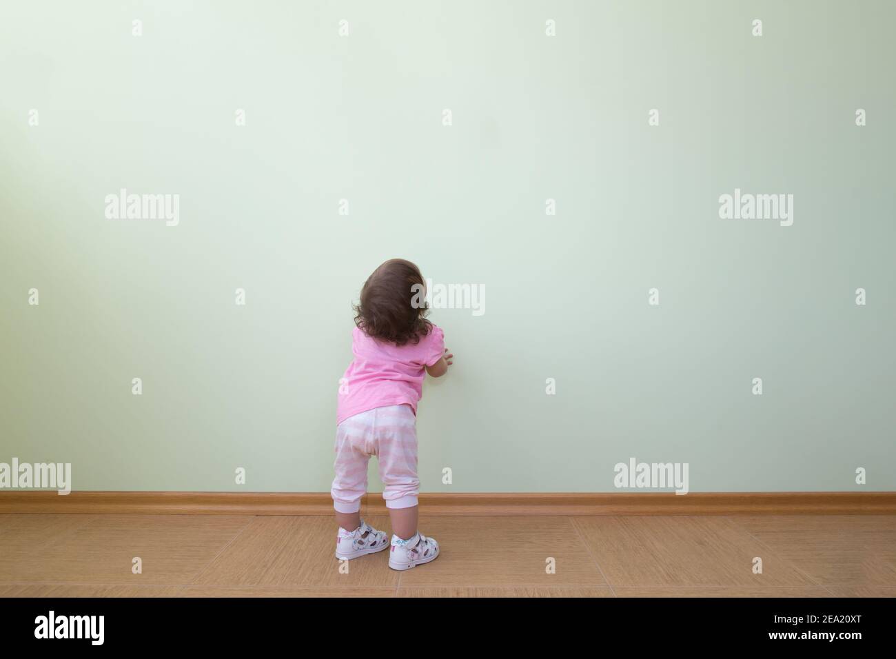 Adorabile bambina in una blusa rosa e pantaloni a righe si trova di fronte a una parete verde e guarda in su. Il concetto di scoperta, il desiderio di conoscenza Foto Stock