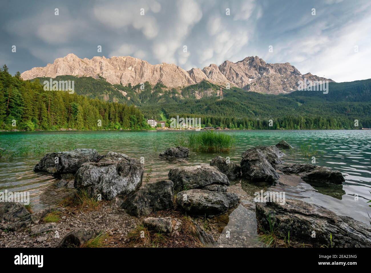 Rocce sulla riva, lago Eibsee di fronte al massiccio Zugspitze con Zugspitze, drammatiche nubi mammaten, Wetterstein, vicino Grainau, Upper Foto Stock