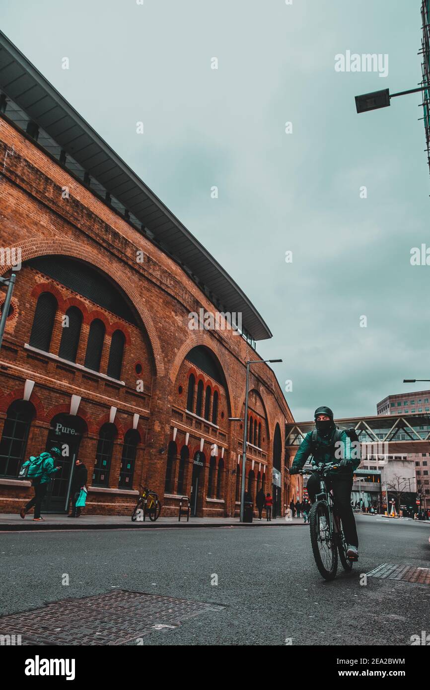 Londra UK Gennaio 2021 immagine grandangolare verticale di un ciclista che passa su una strada londinese, zona della stazione ferroviaria. Drammatica moody inverno girato Foto Stock