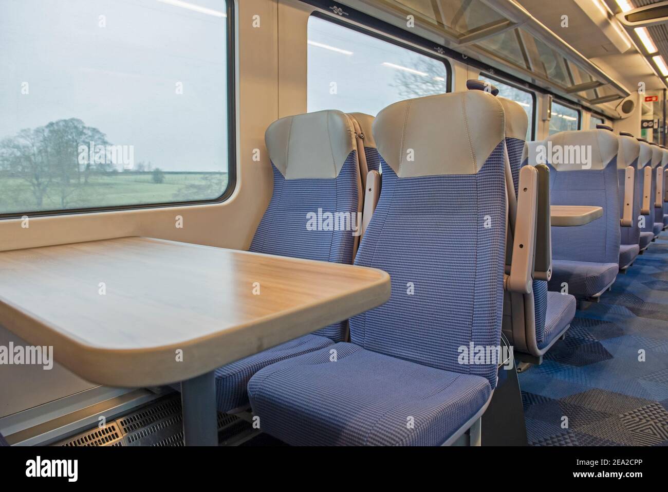 Vista dell'interno di una carrozza vuota deserta per pendolari con file di sedili e tavoli Foto Stock