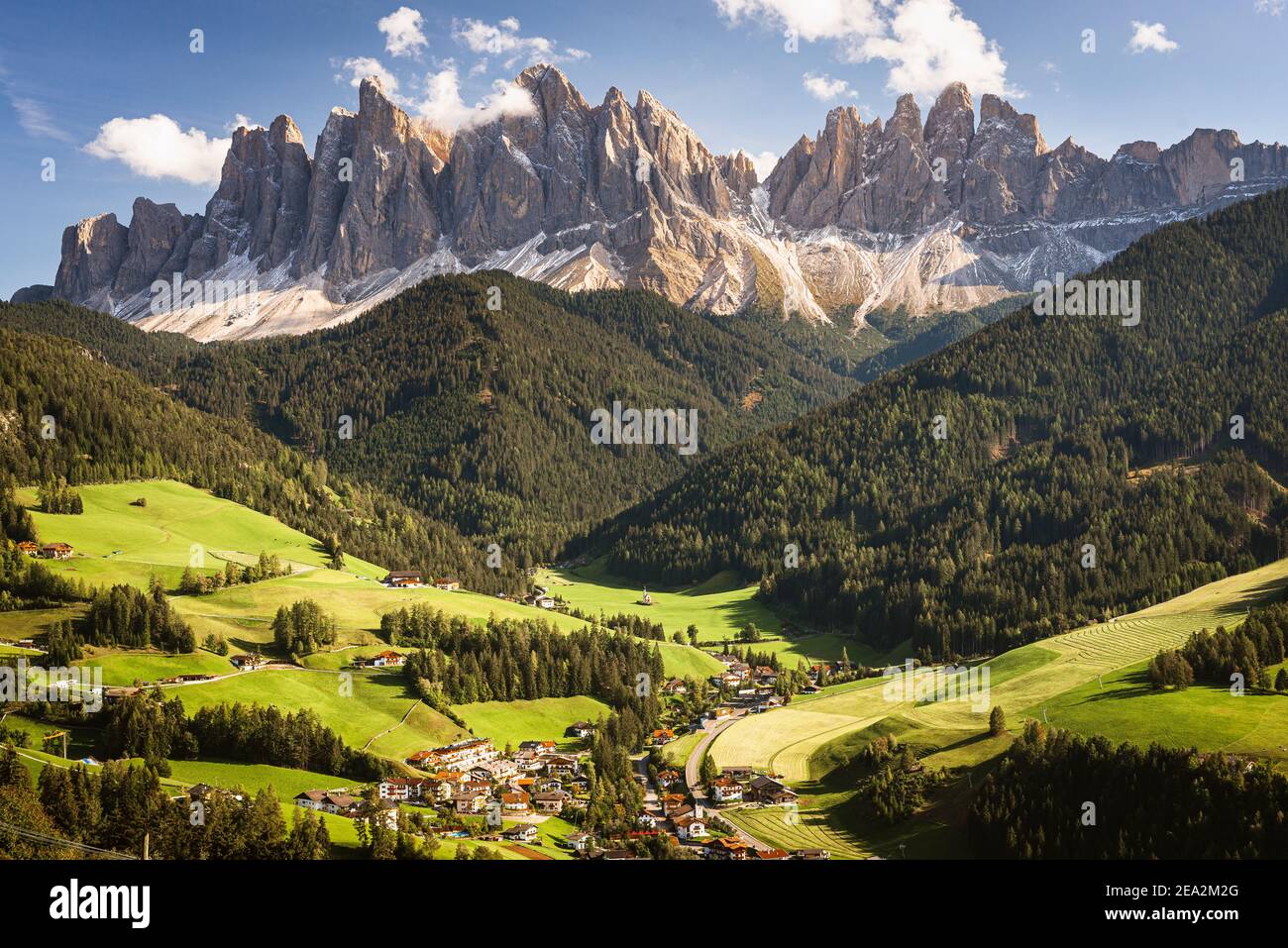 Paesaggio autunnale delle Dolomiti con il villaggio di Villnöss e la Cappella Ranui di fronte ai monti Puez-Odle al sole, Dolomiti, Alto Adige Foto Stock