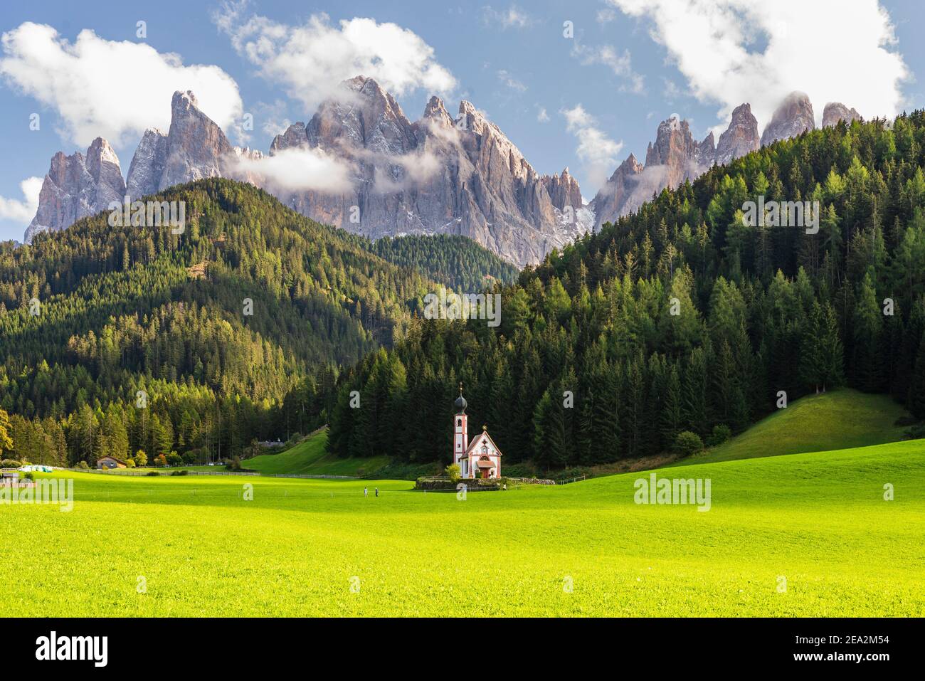 Paesaggio autunnale delle Dolomiti con la Cappella Ranui a Villnöss di fronte alle foreste e rocce delle vette Puez-Odle sotto il sole, Alto Adige Foto Stock