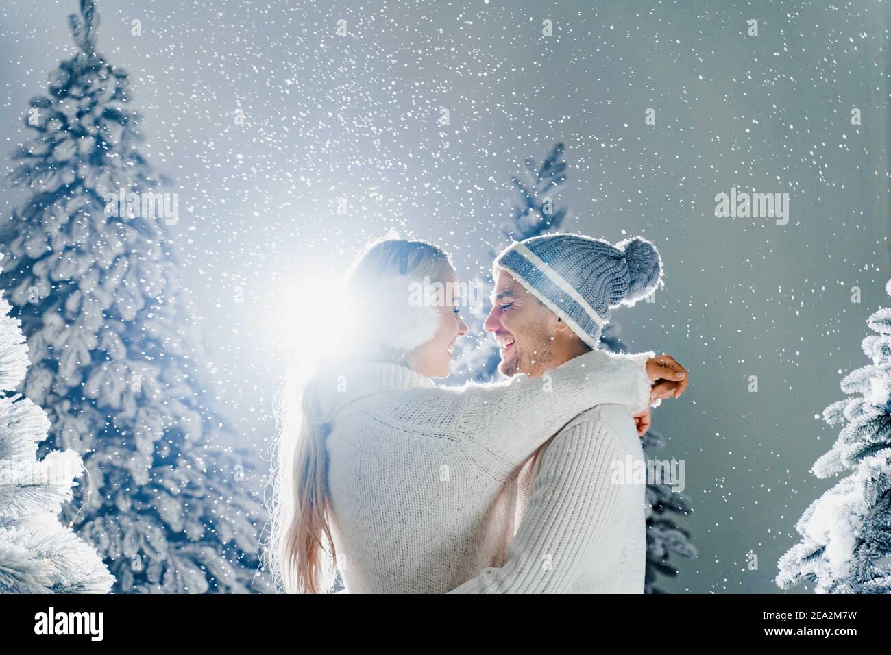 Felice giovane coppia abbracci e sorrisi e la neve cade vicino alberi di  natale alla vigilia della festa di nuovo anno in giorno d'inverno. L'uomo e  la donna smiley si sono stressati