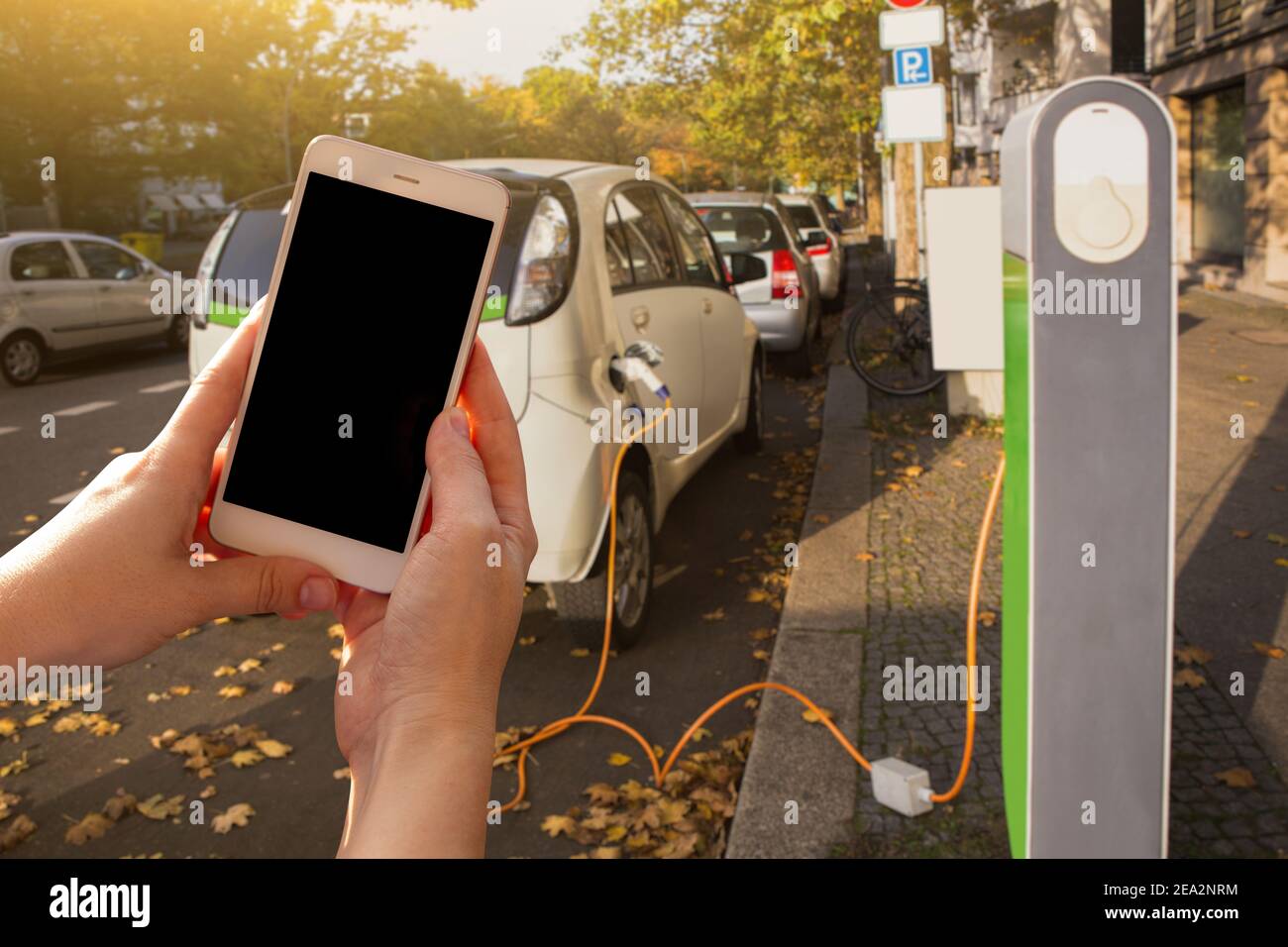 Mani con lo smartphone sullo sfondo di un'auto a noleggio presso la stazione di ricarica per i veicoli elettrici. Condivisione dell'auto. Foto Stock