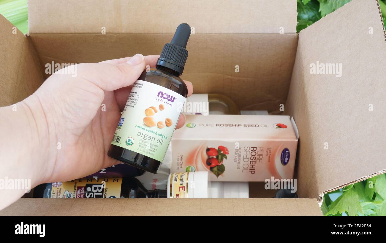 Alicante, Spagna - Gennaio, 2021: Sito web IHerb supplementi e bellezza prodotti naturali scatola disimballaggio. Donna mano che tiene olio di argan Foto Stock